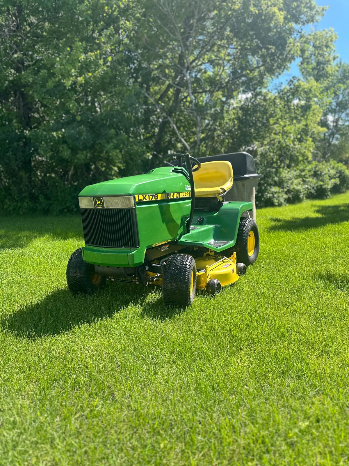 A green lawnmower parked on a green lawn on a sunny day